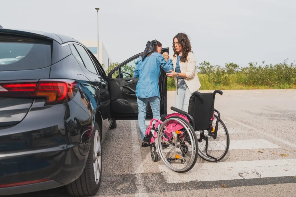 Disabled woman in wheelchair getting out of car with support workers help